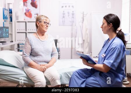 Infermiera sanitaria che dice la diagnosi della donna anziana circa la malattia. Paziente anziano che ha una stazione di conversione con roba medico in clinica privata durante la consultazione. Foto Stock