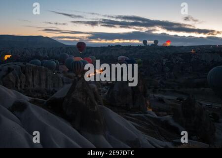 Molti mongolfiera in buia mattina presto prima di alzarsi in cielo. Paesaggio montano in Cappadocia. Colorati palloncini d'aria illuminati tra vulcanico r Foto Stock