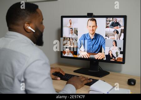 Formazione, webinar online. Un giovane africano guarda sullo schermo con un gruppo di persone diverse. La squadra multirazziale ha riunione in linea Foto Stock