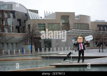 Edimburgo, Scozia, Regno Unito. 3 febbraio 2021. Nella foto: In vista di un dibattito e di un voto al Parlamento scozzese per decidere se il governo scozzese dovrebbe indagare sul finanziamento dei campi da golf scozzesi da parte di Donald Trump, gli attivisti ritrarranno un falso Trump che indossa una testa gigante, una cravatta rossa e porta un cartello con la scritta "Incolosimi!" Al di fuori del Parlamento scozzese. Inoltre trascinerà il suo sacchetto di golf che traboccola con le fatture del dollaro. Credit: Colin Fisher/Alamy Live News Foto Stock