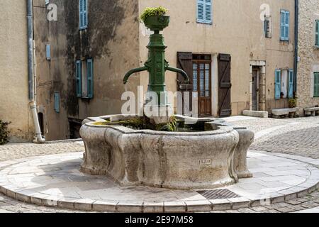 Il villaggio di Mons. Borgo medievale nel sud della Francia. Una piazza nel centro del paese. Una vecchia fontana in ghisa sopra un bacino di pietra. Foto Stock