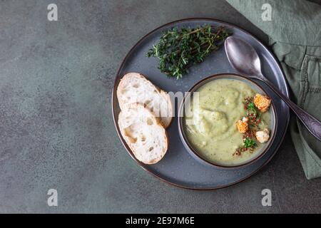 Zuppa di crema di broccoli decorata con timo, crema, cavolfiore arrosto e pane fresco su fondo di cemento verde. Sano cibo vegetariano concetto. Da a. Foto Stock