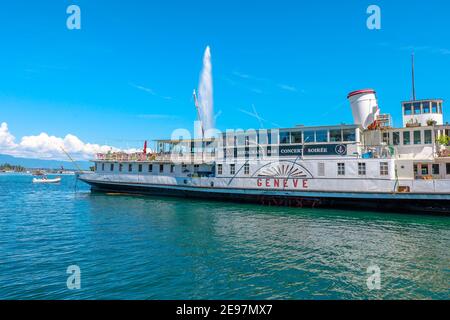 Ginevra, Svizzera - 15 agosto 2020: Battello ristorante nel porto del Lago di Ginevra e fontana Jet d'eau, simbolo della città sullo sfondo. Getto d'acqua Foto Stock