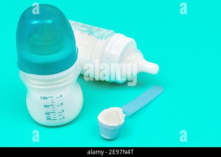 Latte in polvere per il bambino nel misurino vicino ai biberon su sfondo di menta. Concetto di alimentazione del bambino Foto Stock