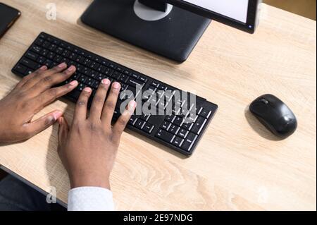 Vista dall'alto mani di un ragazzo afro-americano che digita sulla tastiera del portatile. Primo piano dita di digitazione, programmatore software di sviluppo, giornalista di scrittura Foto Stock