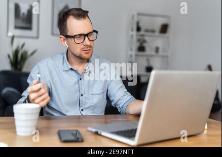 Un giovane che usa un computer portatile in ufficio. Un ragazzo intelligente in occhiali guarda lo schermo con attenzione. Concetto di lavoro remoto Foto Stock