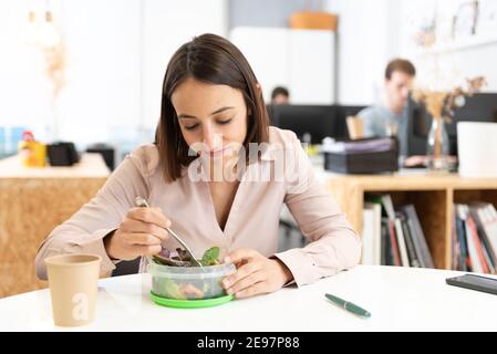 Concetto di cibo sano sul posto di lavoro. Bella donna ispanica che mangia un'insalata in ufficio. Foto Stock
