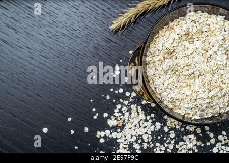 Porridge di farinata d'avena asciutto in un recipiente trasparente su sfondo scuro con una chiodetta con spazio per la copia, vista dall'alto. Foto Stock