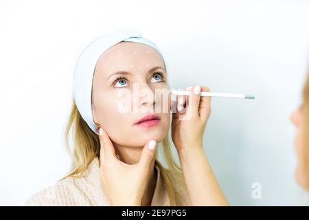 Donna su appuntamento di un estetista. Uno specialista lo esamina e fa le marcature con una matita speciale. Sollevamento viso non chirurgico. Sollevamento SMA Foto Stock