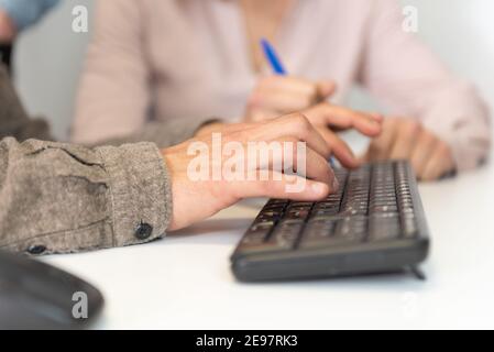 Dettaglio delle mani di un uomo ispanico che scrive su una tastiera nera. Foto Stock