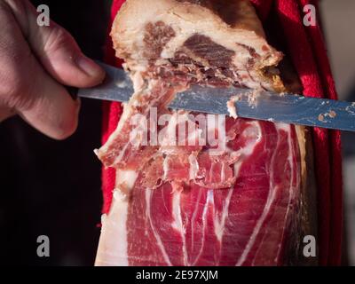 Primo piano orizzontale della mano maschile tagliando una fetta di jamon serrano spagnolo essiccato su tavola di legno. Foto Stock