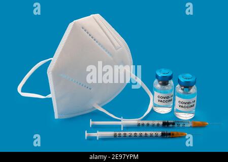 FFP2 - maschera KN95 e vaccino Coronavirus COVID-19. Flaconcini con siringhe con maschera isolata su fondo blu, concetto di protezione composizione con copia Foto Stock