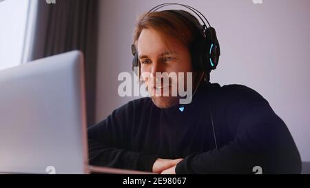 Concetto di lavoro remoto. Giovane uomo con le cuffie che ha una riunione online sul suo laptop. Foto di alta qualità Foto Stock