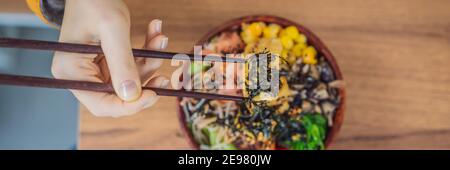 Donna che mangia ciotola di poke organico crudo con riso e verdure primo piano sul tavolo. Vista dall'alto BANNER orizzontale, FORMATO LUNGO Foto Stock