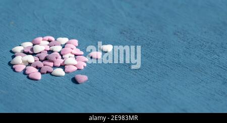 Concetto di celebrazione ed evento speciale con cuori: Vista laterale su piccole caramelle color pastello a cuore su superficie blu con grande spazio copia per speciale Foto Stock