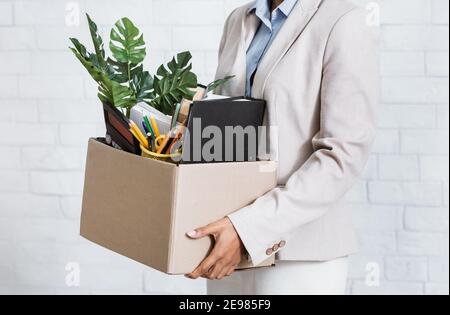 Donna nera irriconoscibile che tiene scatola degli effetti personali, lasciando l'ufficio dopo aver perso il suo lavoro, closeup delle mani Foto Stock