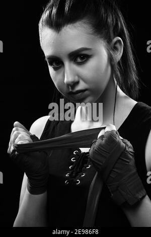 Muay Thai femmina boxer con cinturino al polso. Fitness giovane donna con corpo muscolare preparazione per l'allenamento di boxe su sfondo nero, monocromatico Foto Stock