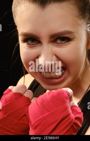 Arrabbiato Muay tailandese pugile in posa di attacco. Fitness giovane donna pugilato formazione su sfondo nero, primo piano Foto Stock