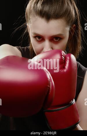 Arrabbiato Muay tailandese pugile in posa di attacco. Fitness giovane donna pugilato formazione su sfondo nero, primo piano Foto Stock