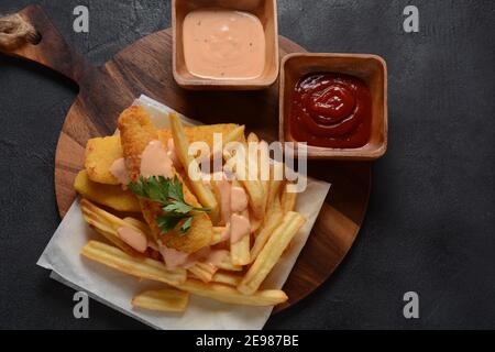 Cibo inglese tradizionale - Pesce e patatine. Filetti di pesce fritti e patatine fritte croccanti serviti con ketchup e salsa di torte fatte in casa. Foto Stock