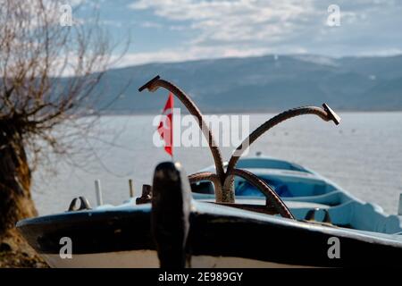 Ancore sulle piccole e blu barche con lago di uluabat e enorme sfondo di montagna. Bandiere turche sulle barche vicino all'albero vecchio e asciutto. Foto Stock