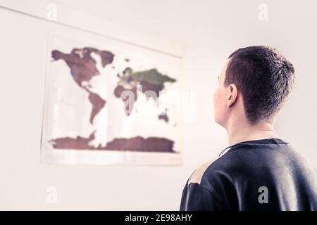 Uomo che guarda una mappa del mondo sul muro. Pensare al cambiamento dell'ambiente, al futuro incerto o ai problemi mondiali. Uguaglianza globale, diritti umani. Foto Stock