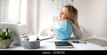 giovane, bella donna architetto è seduto nel suo ufficio e sta tenendo un globo e sogna di viaggiare in tutto il mondo Foto Stock