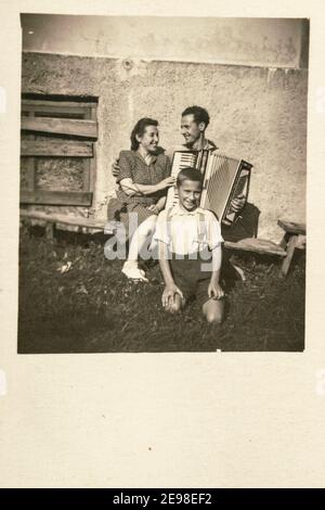 Lettonia - INTORNO agli anni '30: Un colpo di famiglia di coppia sposata con un bambino in portico all'aperto. Uomo con fisarmoniche. Vintage art deco era foto Foto Stock