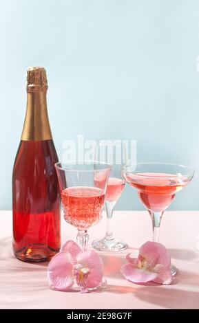 Summer tropicale cocktail vino champagne in un bicchiere diverso con bottiglia decorata fiori di orchidea rosa. Foto Stock