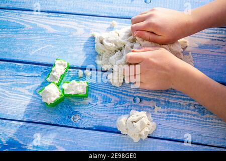 Le mani dei bambini con sabbia cinetica su sfondo di legno blu. Giochi nell'appartamento. Primo piano. Esercizi creativi sulla modellazione della sabbia con i bambini. Foto di alta qualità Foto Stock