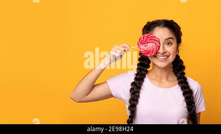 Signora indiana che tiene lollipop, coprendo l'occhio con caramella Foto Stock