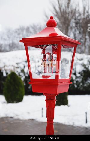 Una vecchia lanterna rossa con decorazione musicale allegra-rotonda di natale in un parco invernale innevato. Inverno innevato. Sfondo di Natale Foto Stock