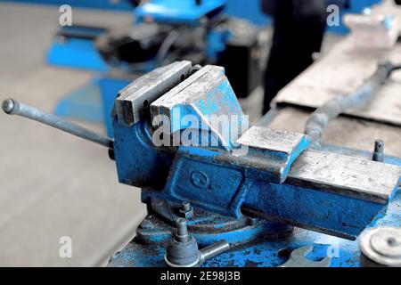 Si tratta di una grande morsa blu in metallo imbullonata al banco di lavoro. Un luogo di lavoro vuoto in officina. Foto Stock