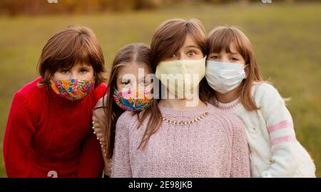 Ritratto di gruppo di bambini in maschere mediche protettive che camminano sopra via della città al tramonto Foto Stock