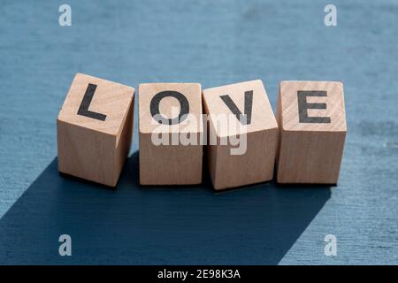 Il concetto di giorno e di emozione felice di Valentin: La parola AMORE scritta con singole lettere cubiche di legno fatte per i giochi da tavolo su superficie testurizzata blu. Foto Stock