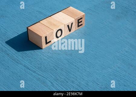 Il concetto di giorno e di emozione felice di Valentin: A sinistra, la parola AMORE scritta con singole lettere cubiche di legno fatte per i giochi da tavolo su superficie testurizzata blu Foto Stock