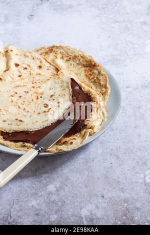 Crepes fresco fatto in casa (o frittelle) con un coltello che sparge cioccolato fondente su una crepe a metà piega. Foto Stock