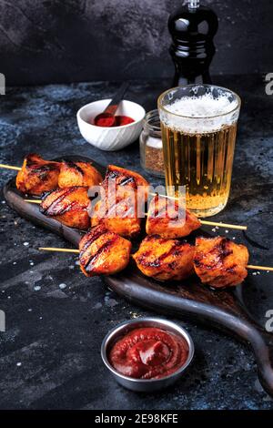 Kebab di pollo facili e deliziosi. Pollo grigliato su spiedini di bambù servito con un drink. Sfondo scuro. Foto Stock