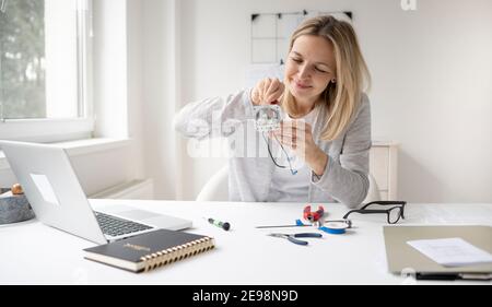 bella, blonde femmina elettricista seduto al tavolo in ufficio che fissa una presa Foto Stock