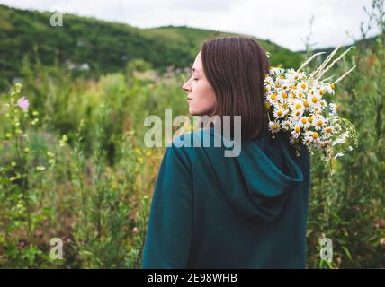 Vista posteriore della ragazza che tiene bouquet di margherite su di lei spalla Foto Stock