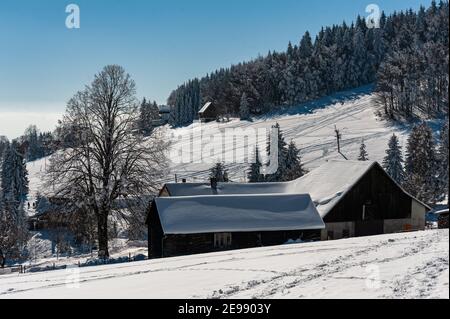 Case sotto la neve nei Vosgi in Francia. - paesaggio invernale in montagna. Alcune case innevate ai margini di una pista da sci. Foto Stock