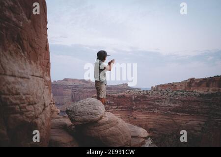 Ragazzo scattando una foto da una scogliera bordo in Canyonlands Parco nazionale Foto Stock