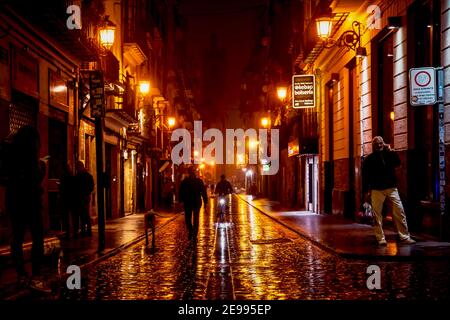 Valencia, Spagna - 18 febbraio 2020: La gente del posto cammina e pedalando attraverso la strada illuminata di arancio 'Carrer de la Bosseria' con vista offuscata sopra Foto Stock