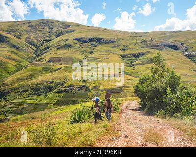 Sendrisoa, Madagascar - 28 aprile 2019: Piccolo gruppo di malgascio ignoti locali a piedi a casa su collina dopo aver lavorato a campi, sulla strada della polvere rossa, fiel Foto Stock