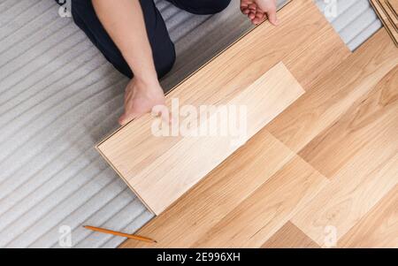 Installazione del pavimento laminato, vista dettagliata dall'alto su mani di uomo che tengono la piastrella di legno, montandola, su strato di base in schiuma bianca Foto Stock