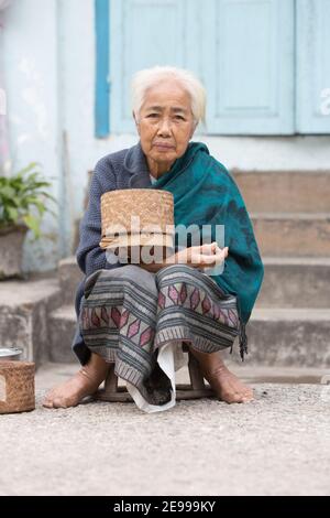 Luang Prabang, Laos Vecchia donna che consegna il riso a Tak Bat o la processione mattutina del monaco. Foto Stock