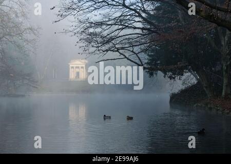 Un piccolo tempio neoclassico e boschi che si riflettono in uno stagno in una mattinata nebbiosa al Parco di Monza, Italia Foto Stock