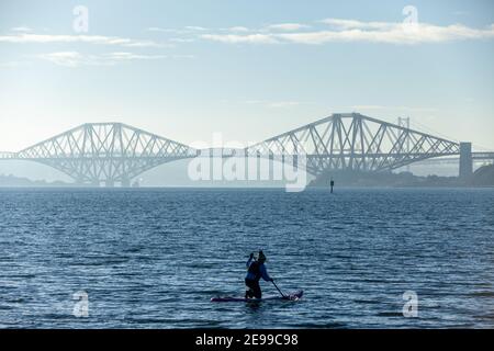 Un paddle boarder godendo del sole invernale sul Firth of Forth vicino al Forth Bridge, al Saint Davids Bay Fife Foto Stock