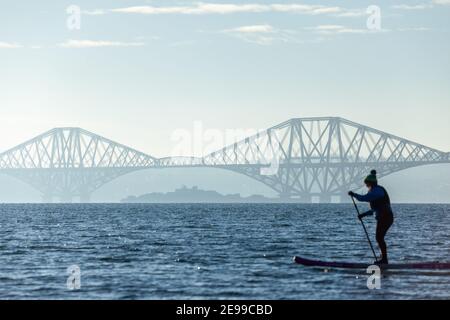 Un paddle boarder godendo del sole invernale sul Firth of Forth vicino al Forth Bridge, al Saint Davids Bay Fife Foto Stock