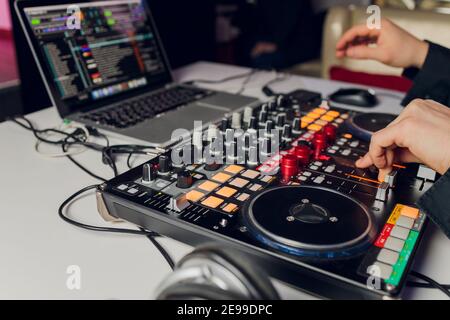 La mano del DJ sul computer portatile e la console di mixaggio che controlla impostazioni audio Foto Stock